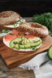 Delicious bagel with cream cheese, salmon, avocado and microgreens on wooden table