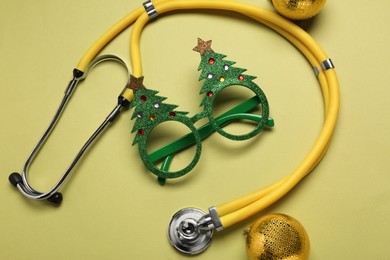 Greeting card for doctor with stethoscope and Christmas decor on green background, flat lay