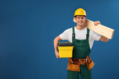 Photo of Handsome carpenter with wooden planks and tool box on blue background. Space for text