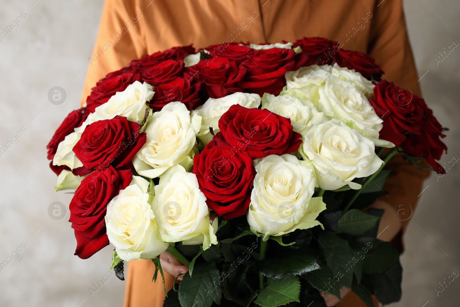 Photo of Woman holding luxury bouquet of fresh roses on beige background, closeup