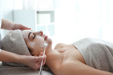 Cosmetologist applying mask on client's face in spa salon