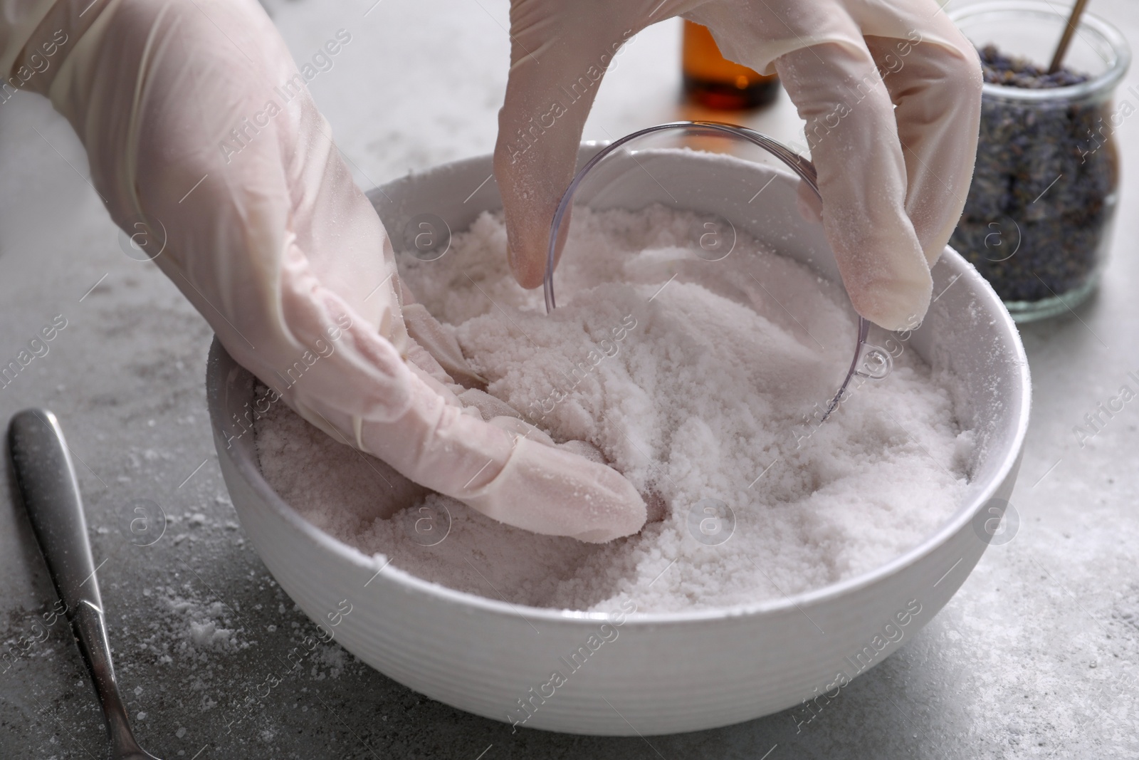 Photo of Woman in gloves making bath bomb at grey table, closeup