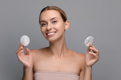 Photo of Removing makeup. Smiling woman with cotton pads on grey background