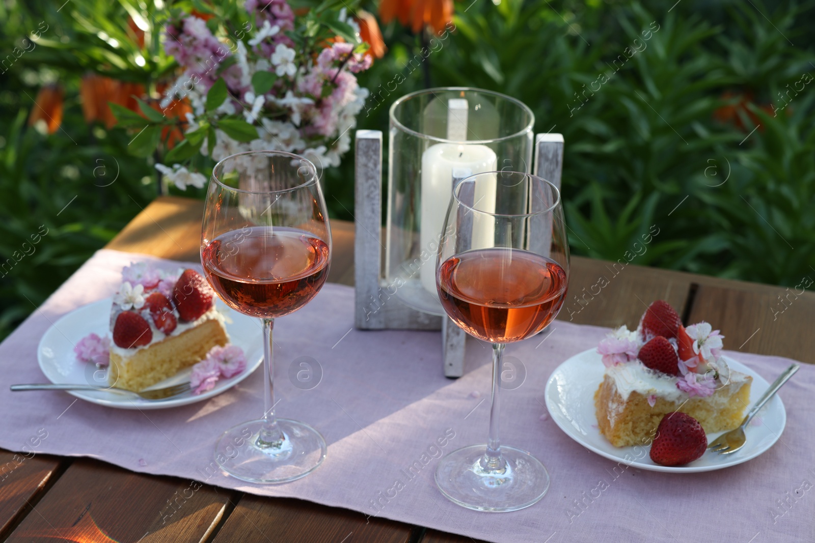 Photo of Vase with spring flowers, wine and cake on table served for romantic date in garden