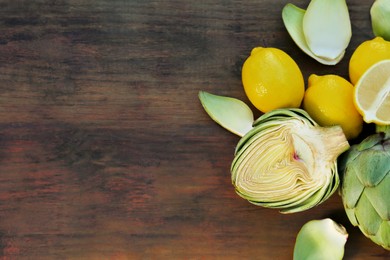 Photo of Artichokes and lemons on wooden table, flat lay. Space for text