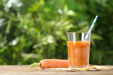 Photo of Glass of carrot drink on wooden table against blurred background, space for text