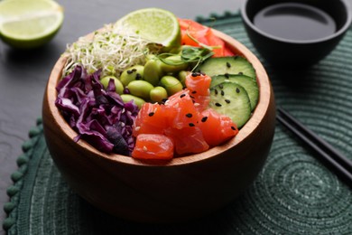 Photo of Delicious poke bowl with vegetables, fish and edamame beans on black table, closeup