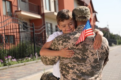 Photo of Soldier and his little son with flag of USA hugging outdoors