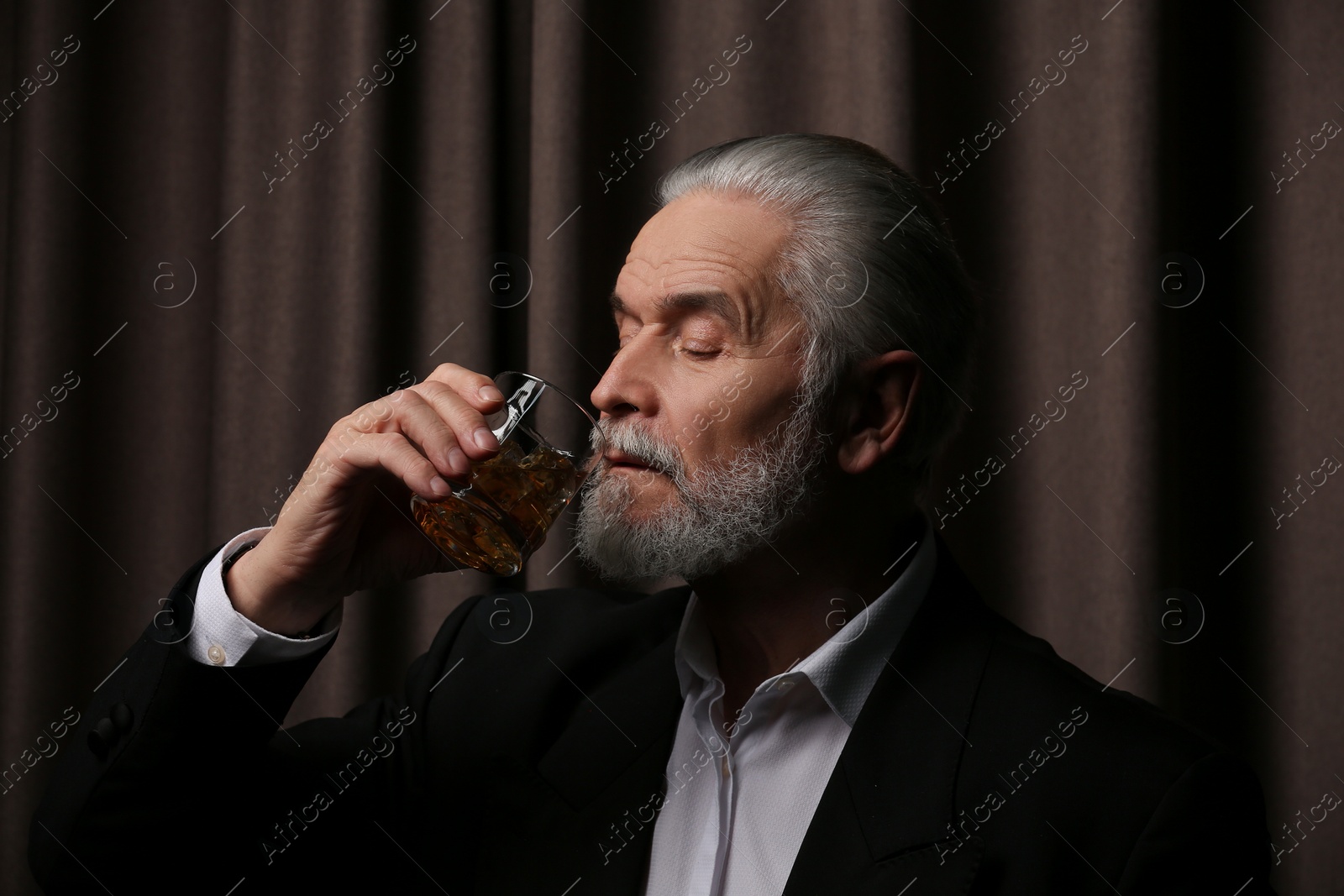 Photo of Senior man in suit drinking whiskey on brown background