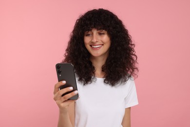 Happy young woman looking at smartphone on pink background