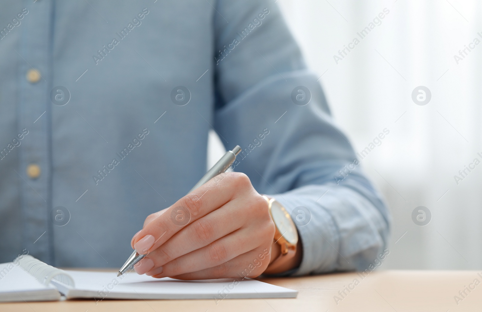 Photo of Woman writing in notebook at wooden table, closeup