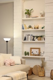 Sofa near shelves with different decor in room. Interior design