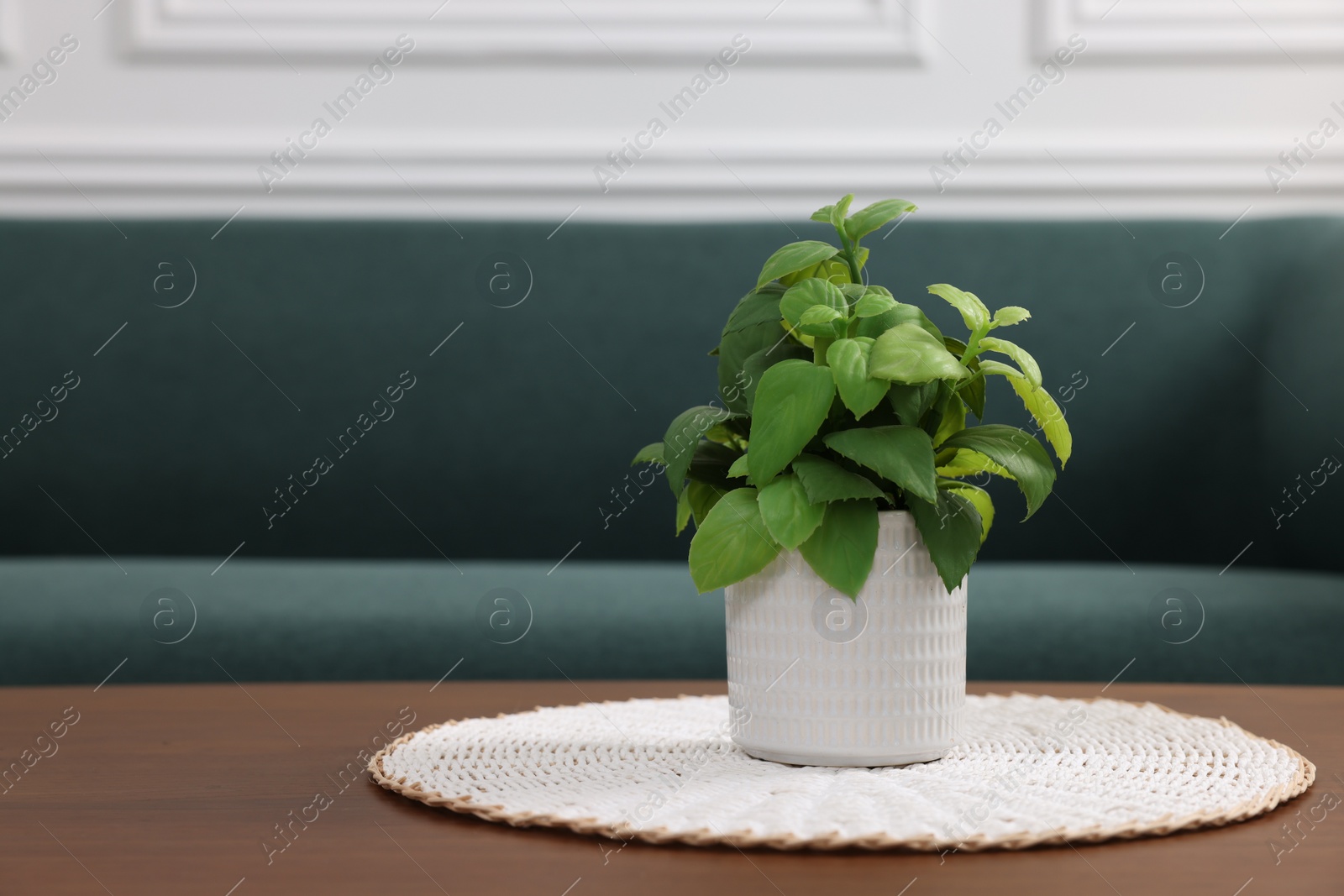 Photo of Green artificial plant in pot on wooden table indoors, space for text