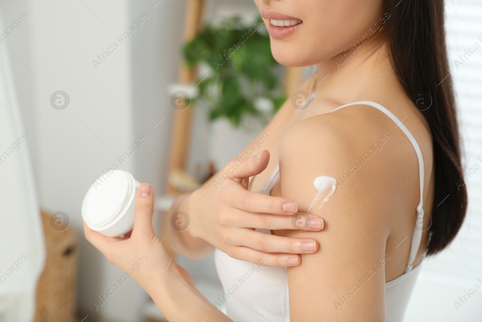 Photo of Young woman applying body cream on shoulder in room, closeup. Space for text