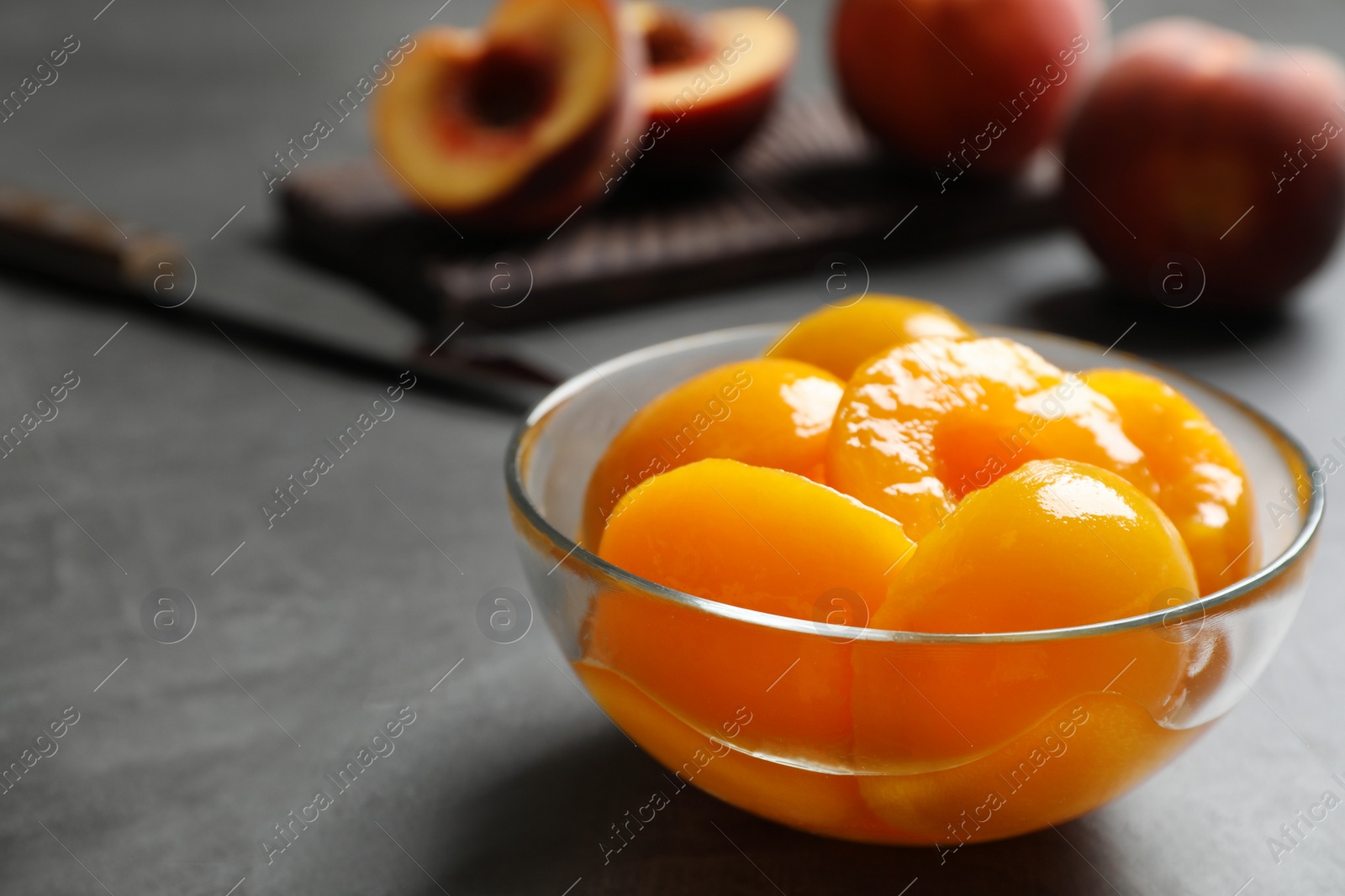 Photo of Glass bowl with conserved peach halves on grey table. Space for text