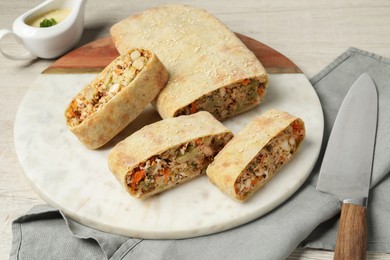 Cut tasty strudel with chicken, vegetables and knife on light wooden table