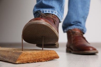 Photo of Careless man stepping on nails in wooden plank indoors, closeup