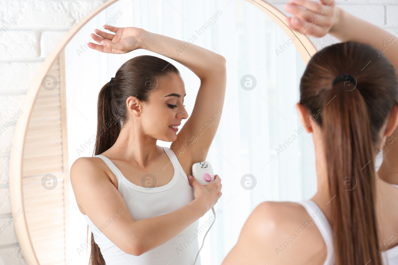 Photo of Young woman doing armpit epilation procedure near mirror at home