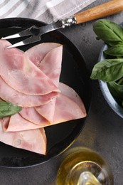 Tasty ham with basil, olive oil and carving fork on grey table, flat lay