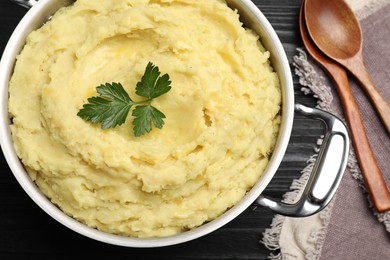 Photo of Pot of tasty mashed potatoes with parsley on black wooden table, flat lay