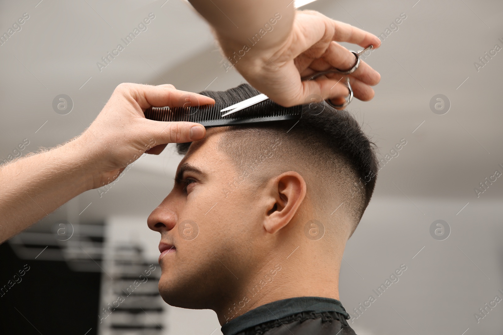 Photo of Professional barber making stylish haircut in salon, closeup