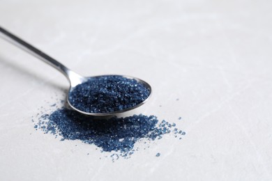 Spoon with blue food coloring on light grey table, closeup. Space for text