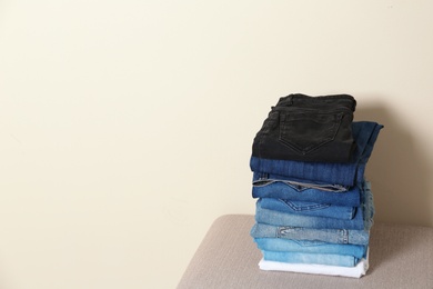 Stack of different jeans on ottoman against light background. Space for text