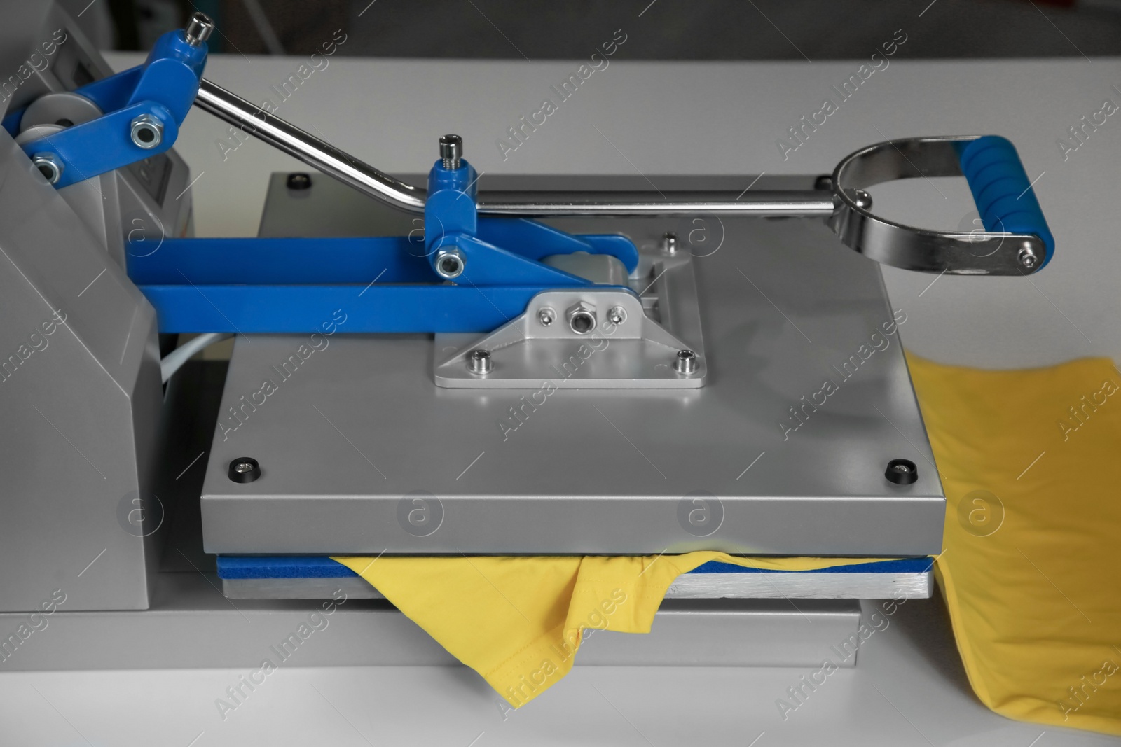 Photo of Printing logo. Heat press with yellow t-shirt on white table