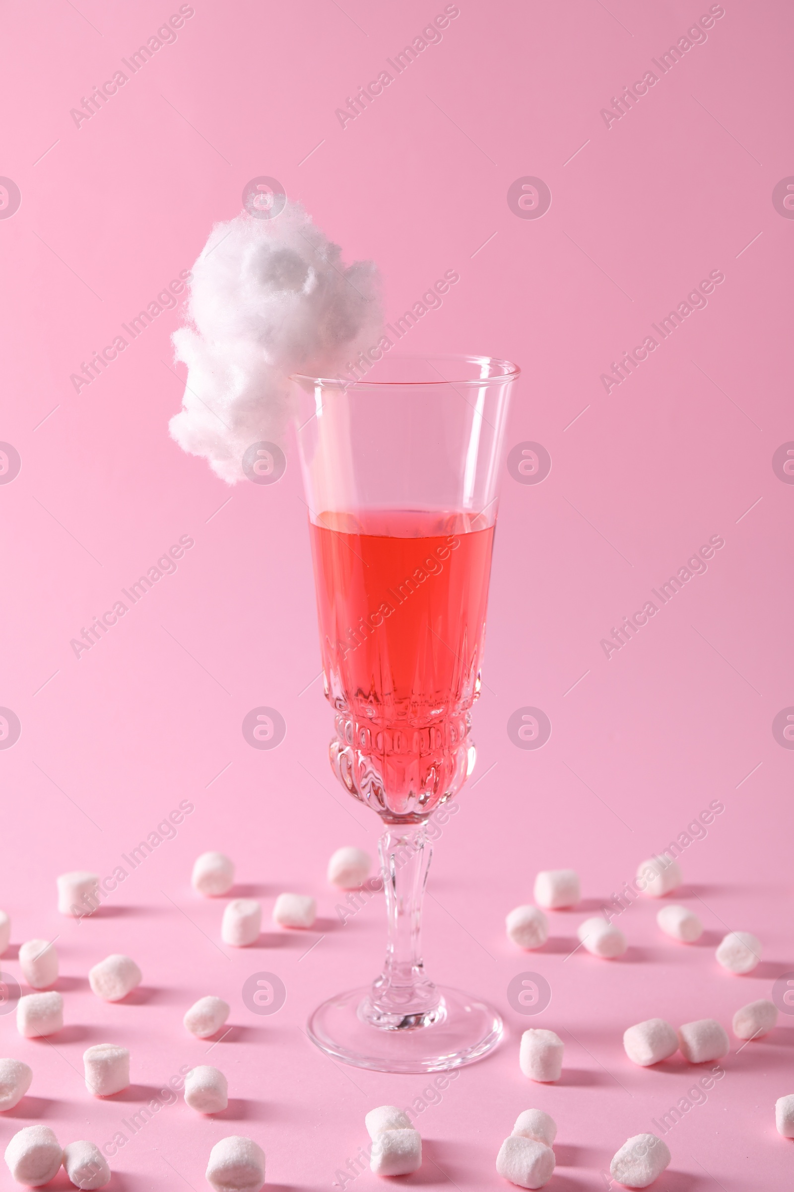 Photo of Tasty cocktail in glass decorated with cotton candy and marshmallows on pink background