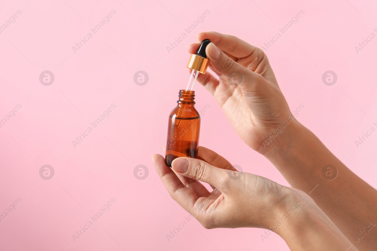 Photo of Woman with bottle of cosmetic serum and dropper on pink background, closeup. Space for text