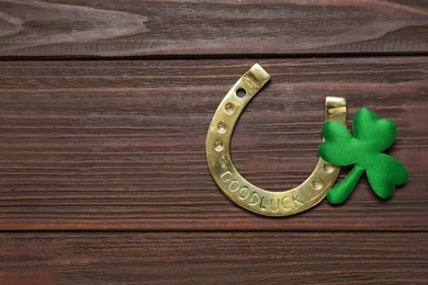 Photo of Clover leaf and horseshoe on wooden table, flat lay with space for text. St. Patrick's Day celebration