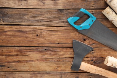 Saw with light blue handle, axe and firewood on wooden background, flat lay. Space for text