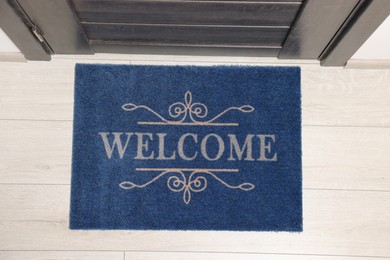 Photo of Blue doormat with word Welcome on white floor near entrance, top view