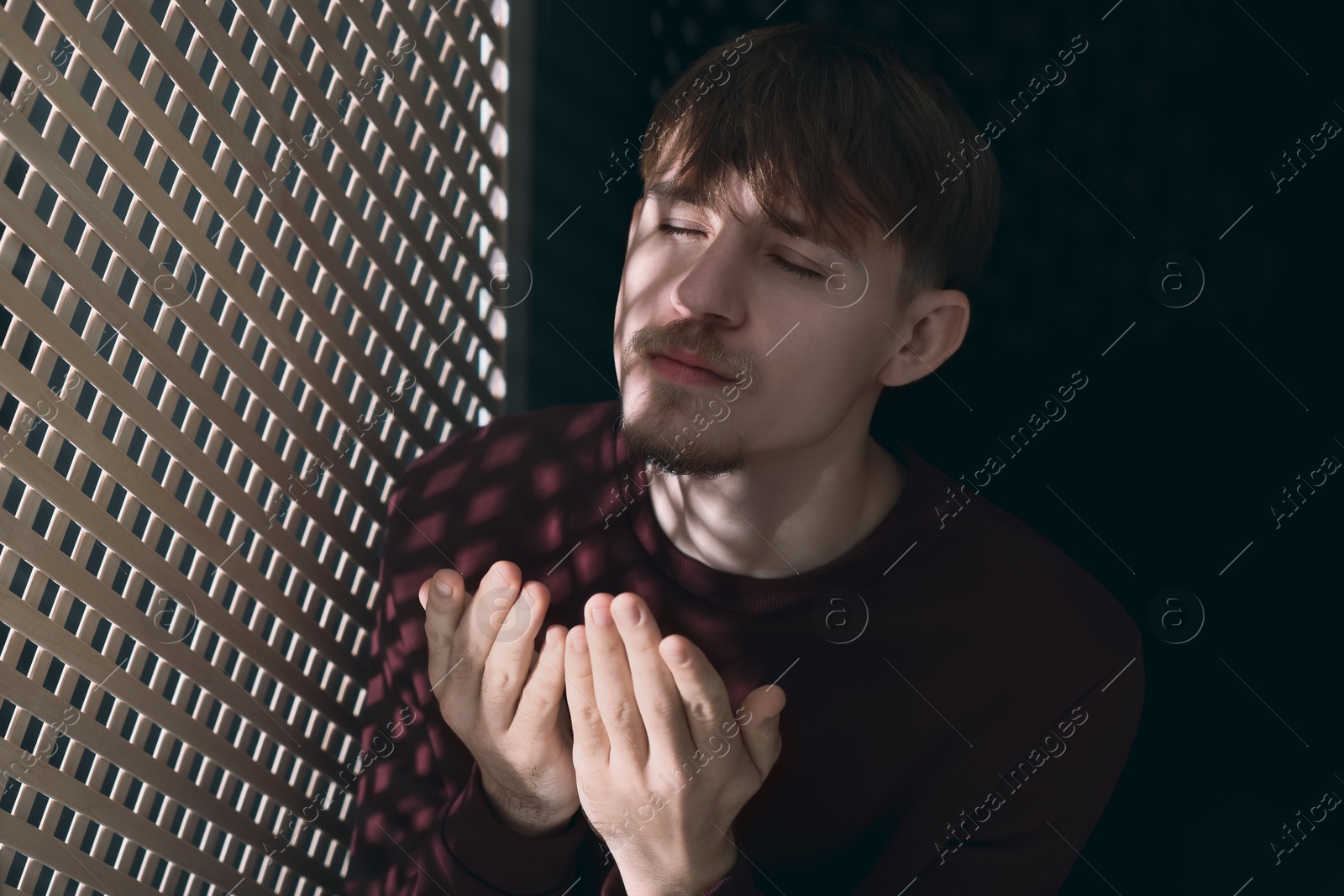 Photo of Man praying during confession near wooden window in booth