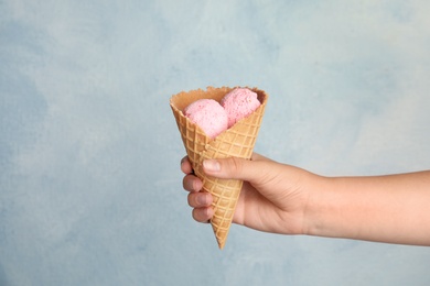 Photo of Woman holding delicious ice cream in wafer cone on light blue background, closeup