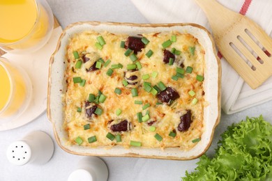 Photo of Tasty sausage casserole with green onions in baking dish served on white table, flat lay