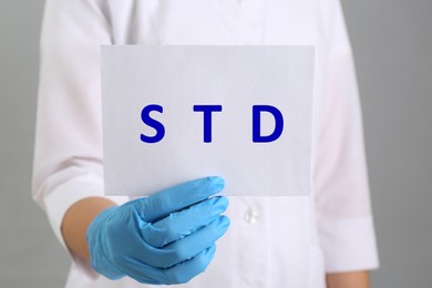 Doctor holding sheet of paper with abbreviation STD on grey background, closeup