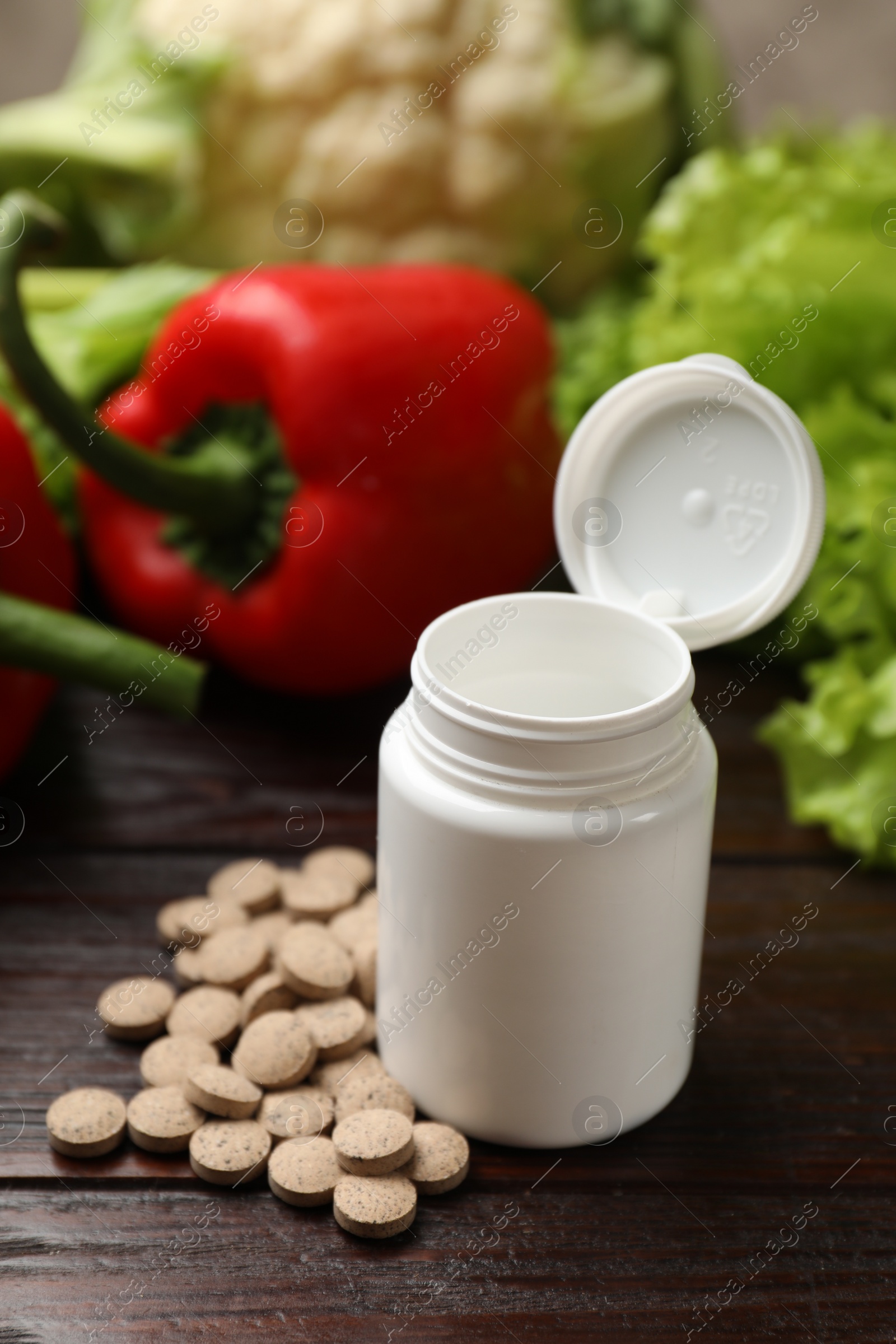 Photo of Dietary supplements. Plastic bottle, pills and food products on wooden table