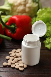 Photo of Dietary supplements. Plastic bottle, pills and food products on wooden table