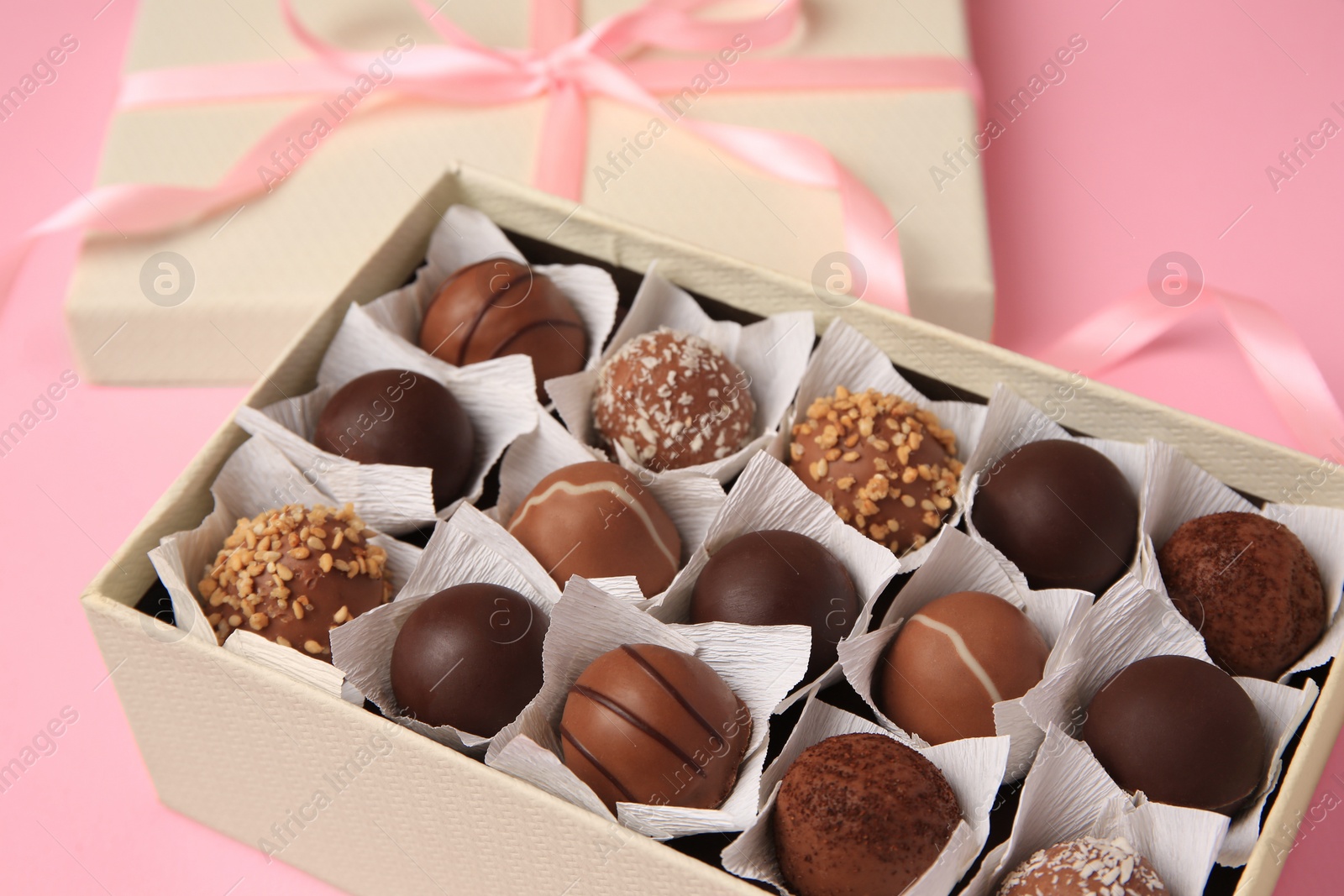 Photo of Box of delicious chocolate candies on pink background, closeup