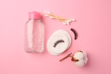 Bottle of makeup remover, cotton flower, pads, swabs and false eyelashes on pink background, flat lay