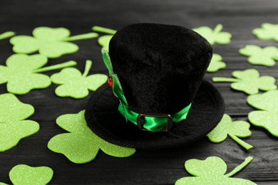 Photo of Leprechaun's hat and decorative clover leaves on black wooden background. St. Patrick's day celebration