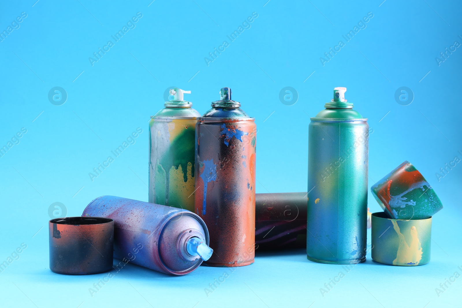 Photo of Many spray paint cans and caps on light blue background