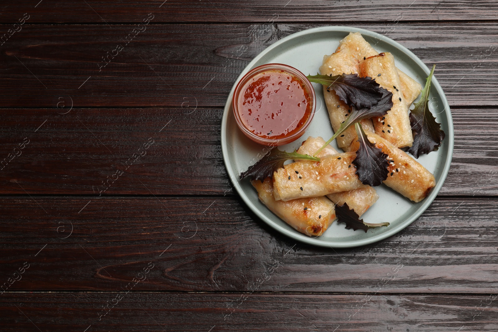 Photo of Tasty fried spring rolls, lettuce and sauce on wooden table, top view. Space for text