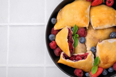 Photo of Bowl with delicious samosas, berries and mint leaves on white tiled table, top view. Space for text