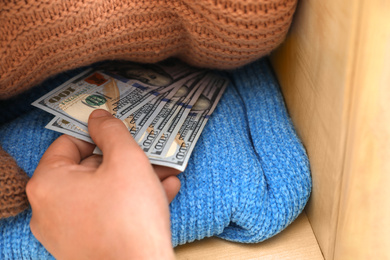 Man hiding money between clothes in wardrobe, closeup. Financial savings