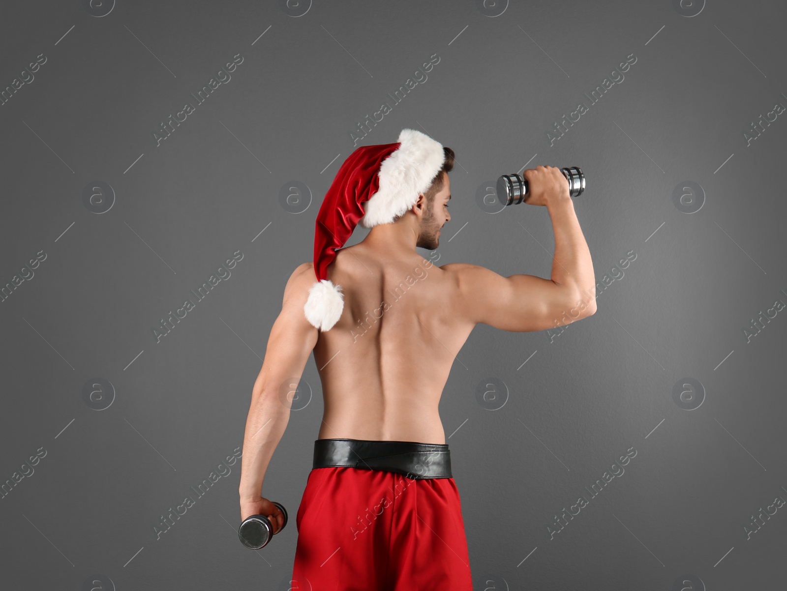 Photo of Shirtless sexy young Santa Claus with dumbbells on color background