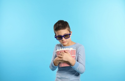 Boy with 3D glasses and popcorn during cinema show on color background