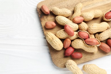 Photo of Fresh unpeeled peanuts on white wooden table, top view. Space for text