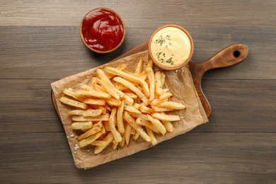 Delicious french fries served with sauces on wooden table, flat lay